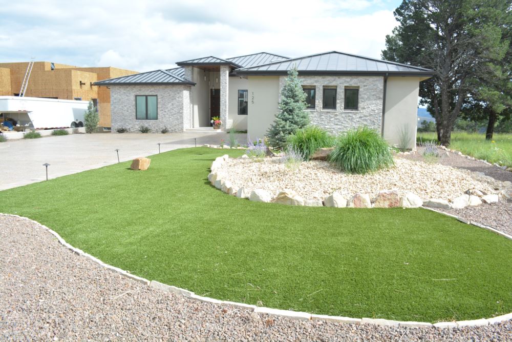 Custom artificial turf backyard next to a curved stone patio and surrounded by bushes.